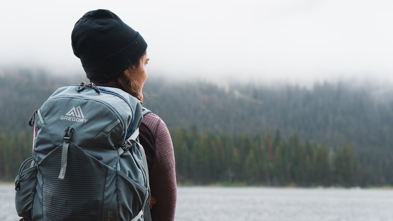 Woman with backpack overlooking a foggy forest by a lake, capturing tranquility and exploration.