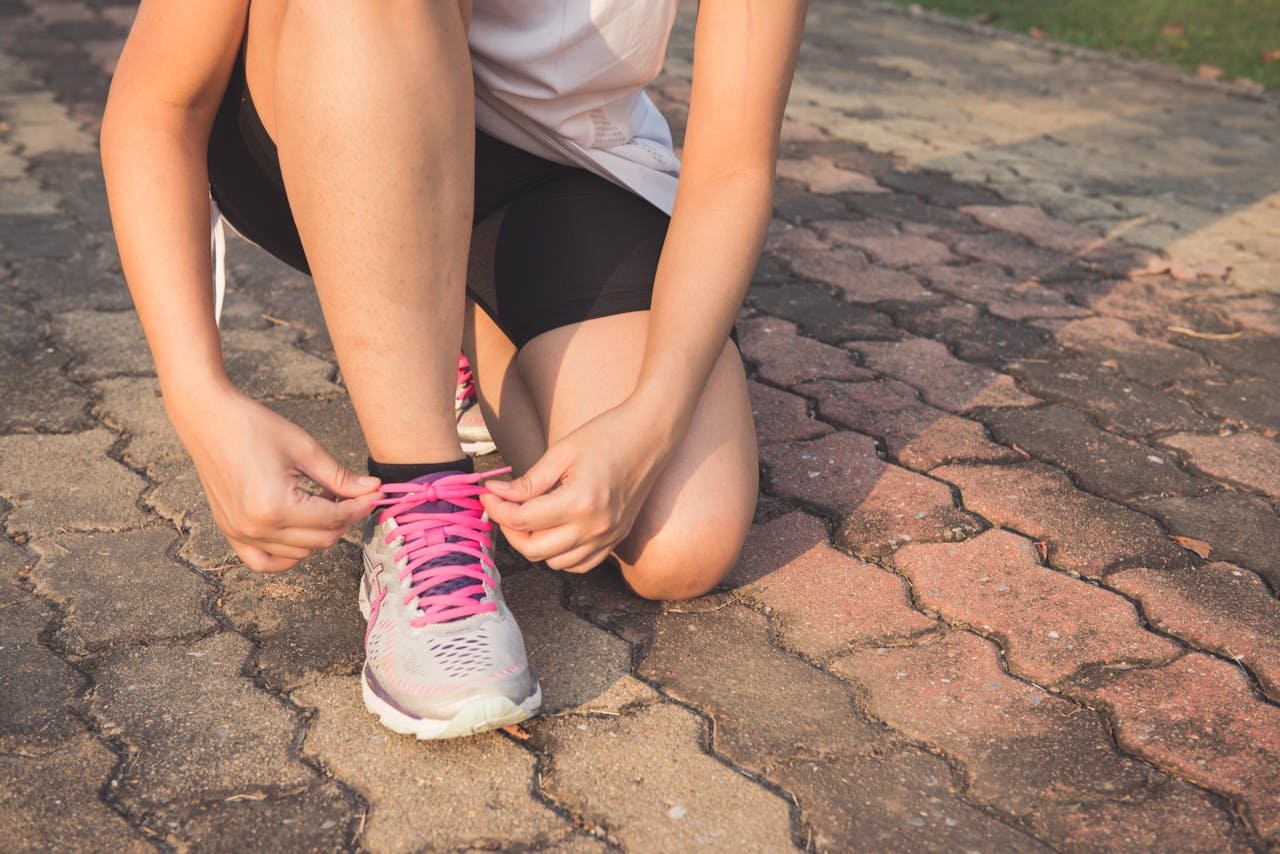 our-story Adult woman tying pink laces on running shoes outdoors. Focuses on fitness and lifestyle.